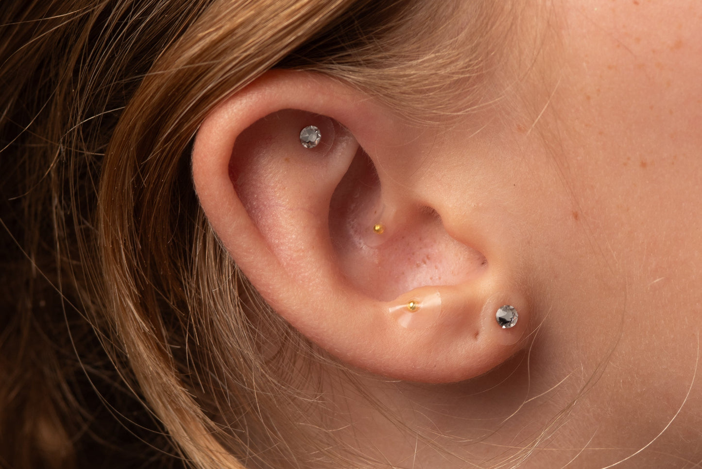 Close-up of a woman's ear with ear seeds against a neutral background