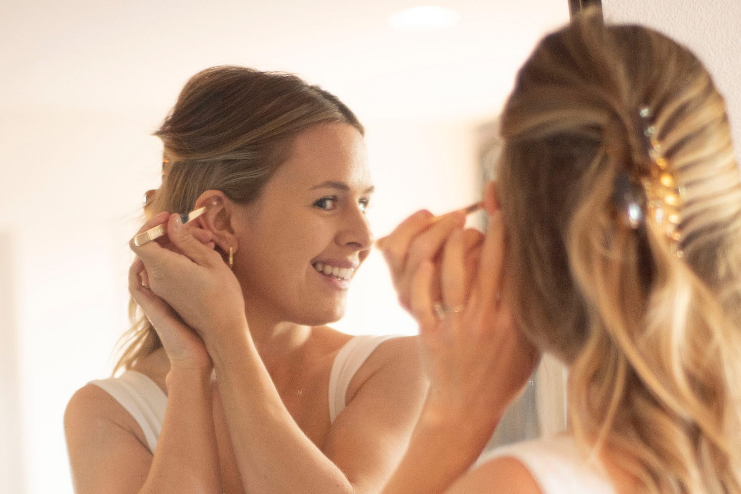 Girl placing ear seeds on her ear while looking into a mirror.